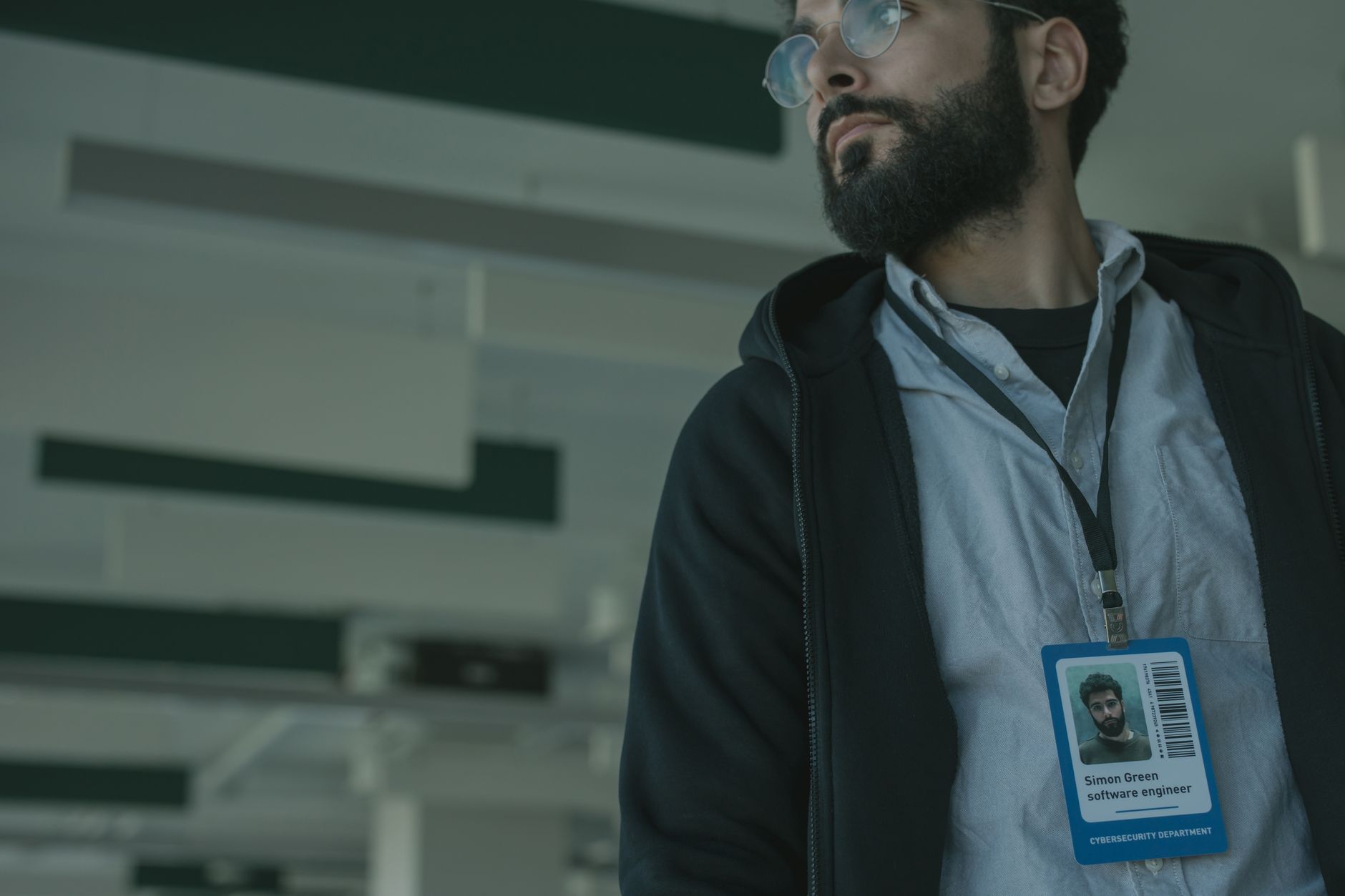 Male software engineer with glasses and name badge in a contemporary office interior.