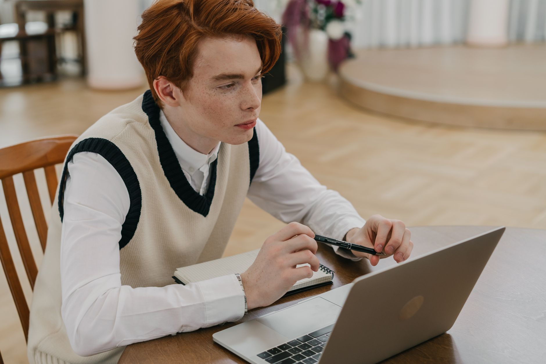 Focused young man engaged in online learning at home with a laptop and notebook.