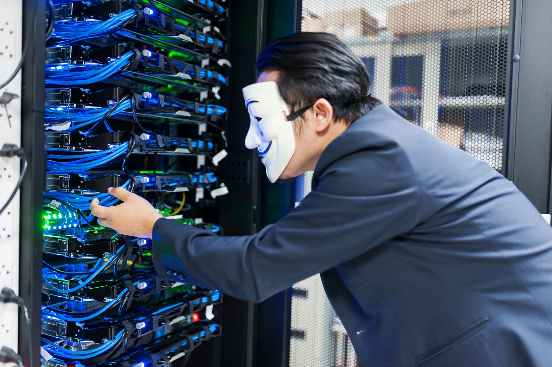 Masked individual interacting with server racks, symbolizing cybersecurity threats.
