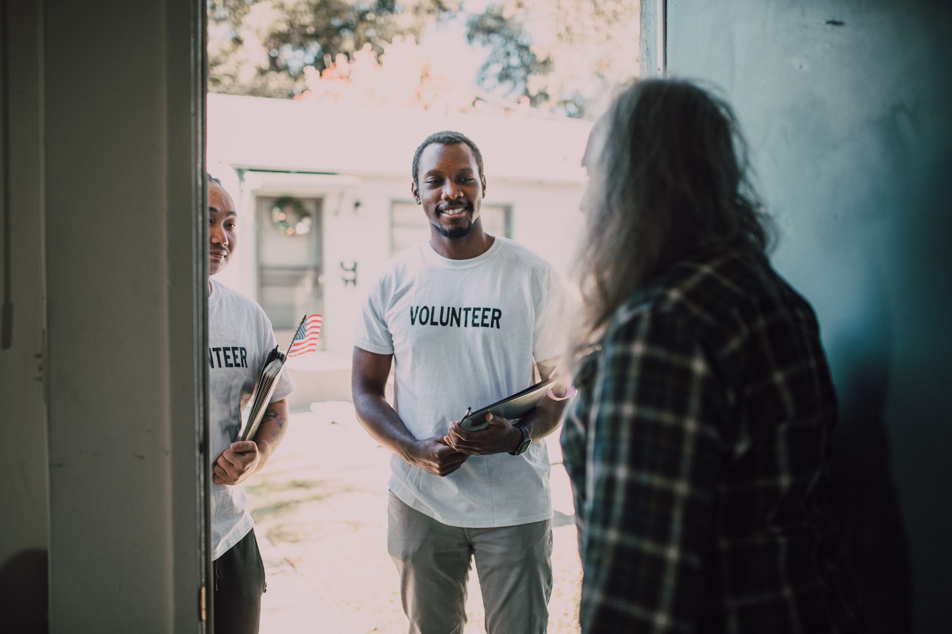 Two diverse volunteers, holding documents, visit a home to offer community support and services.