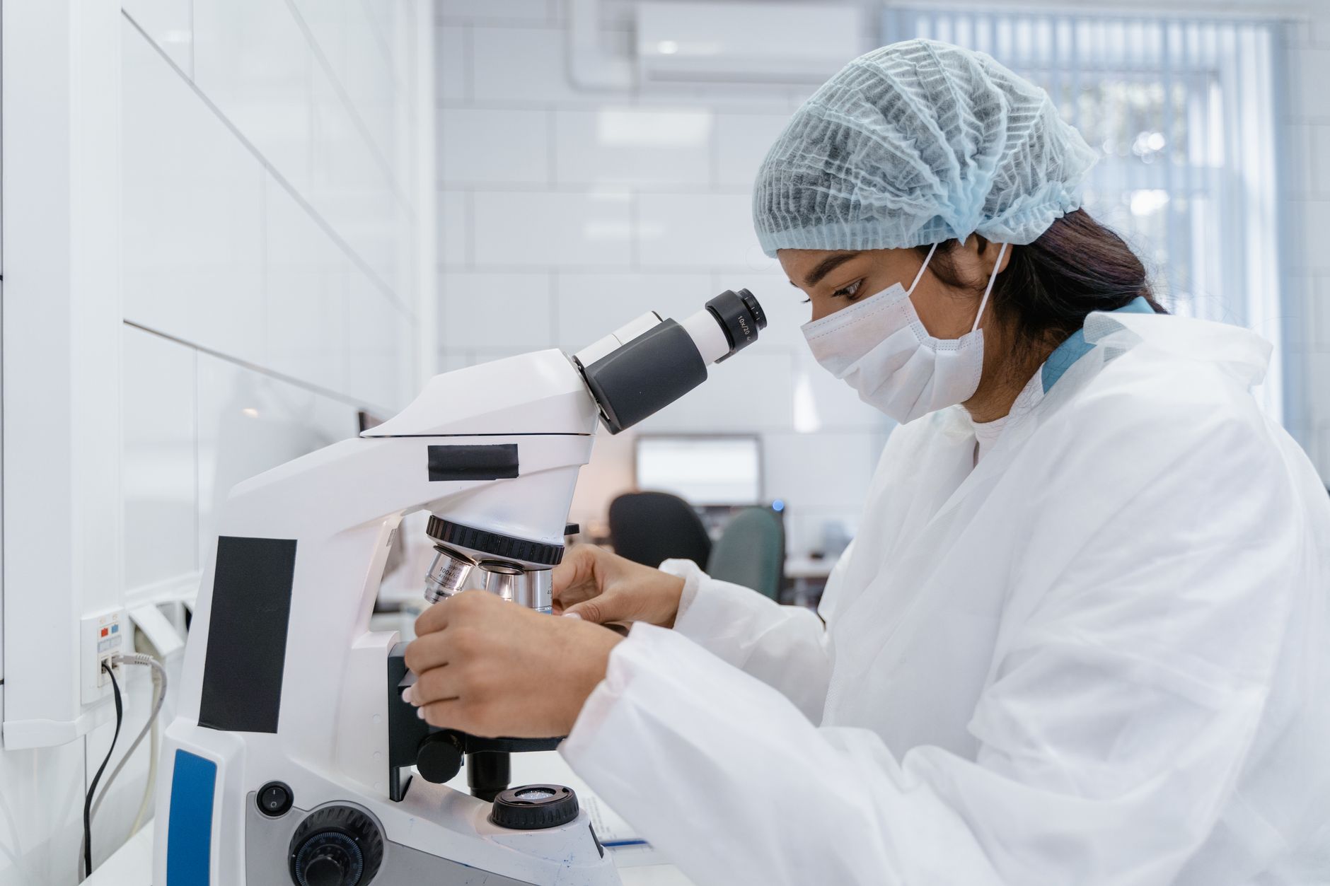 A female scientist wearing protective gear analyzes samples using a microscope in a modern laboratory.