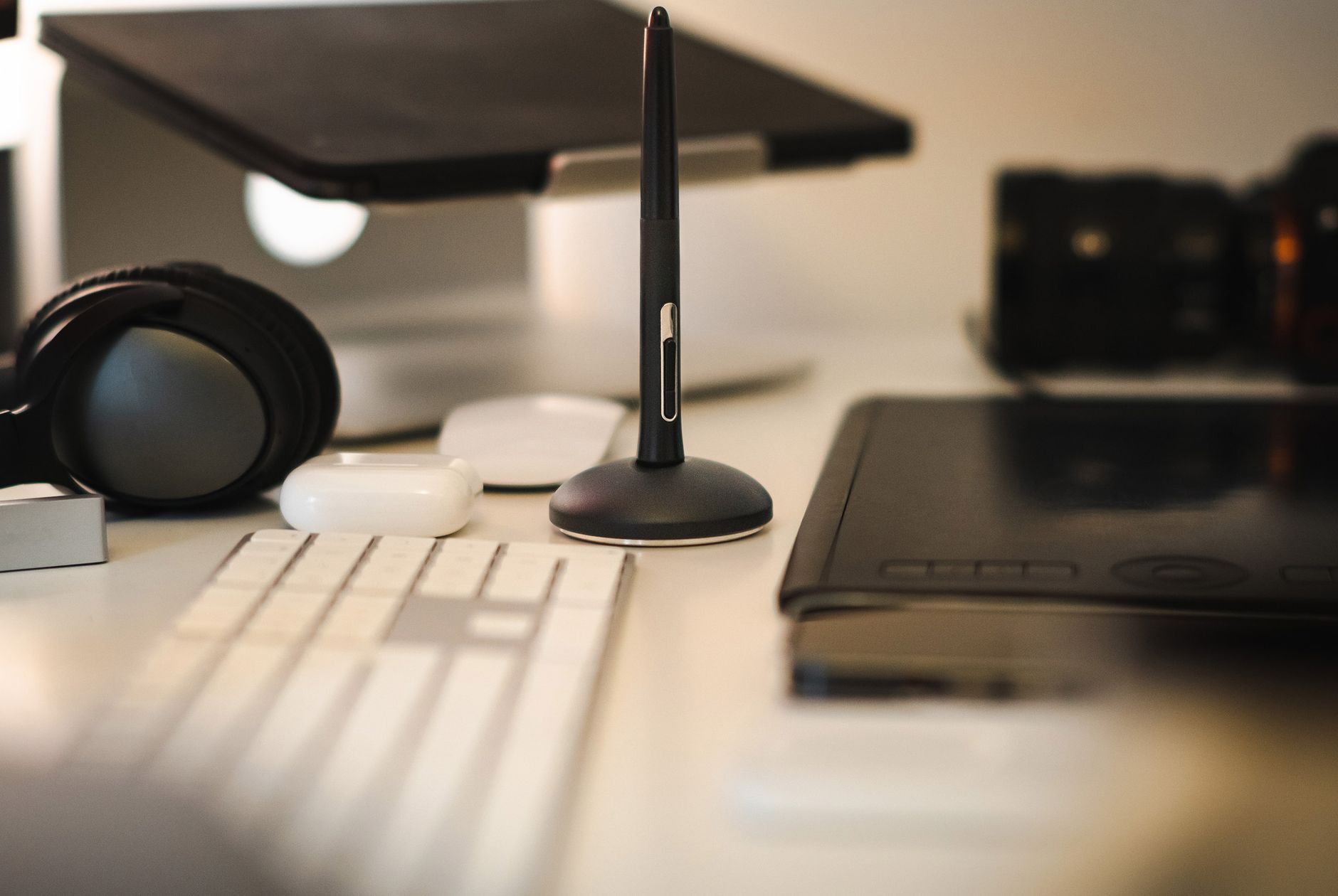 A sleek modern workspace featuring a graphic tablet, stylus, keyboard, headphones, and camera.