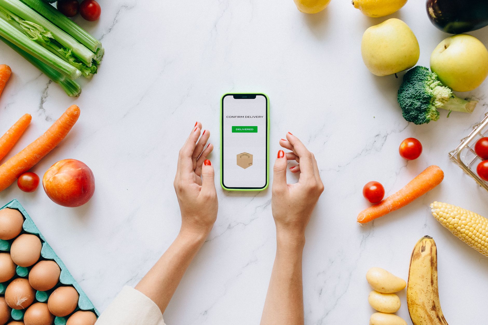 Hands holding smartphone displaying online grocery order amidst fresh vegetables and fruits.