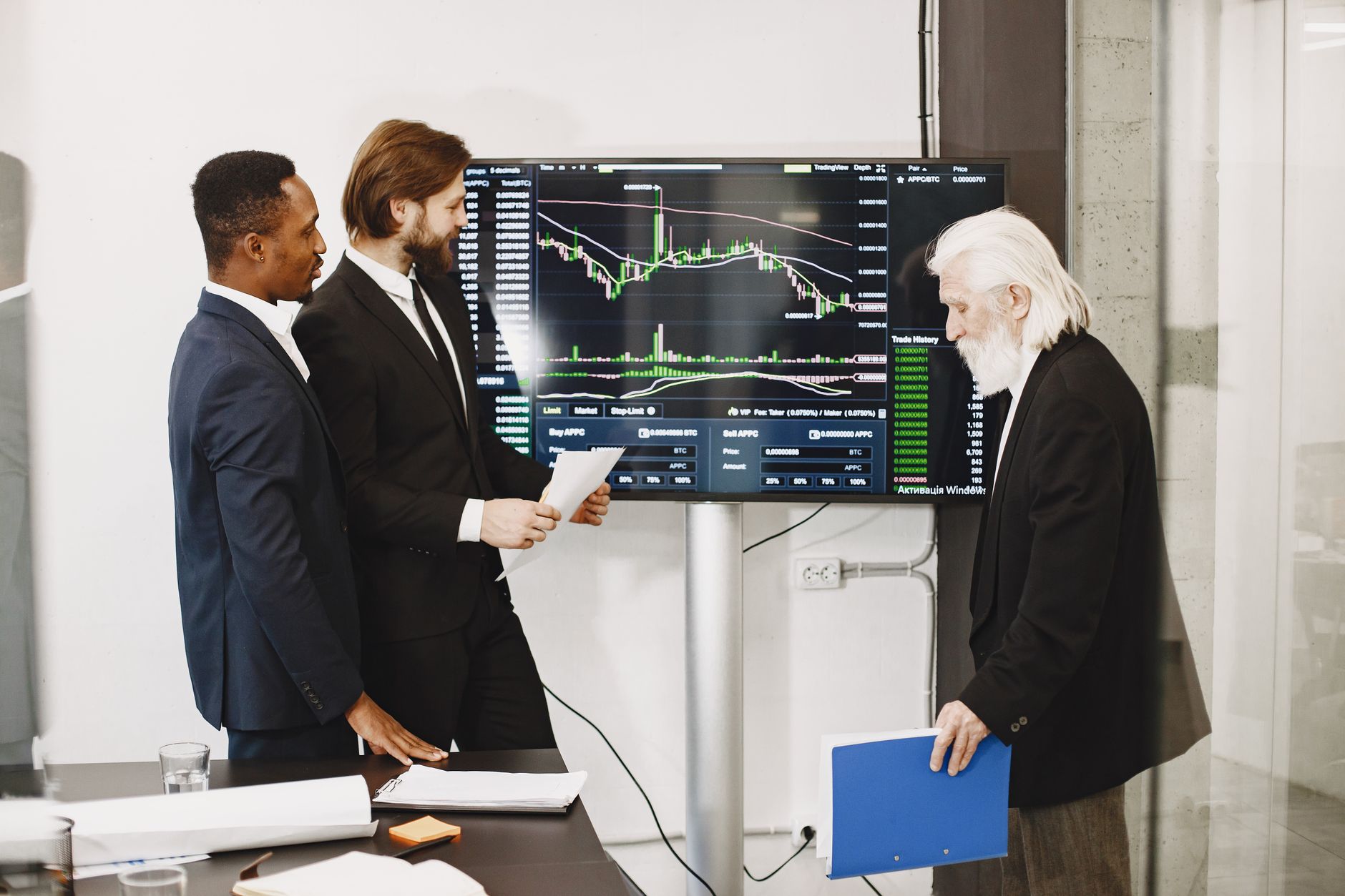 Three businessmen analyzing financial charts on a screen in an office setting.