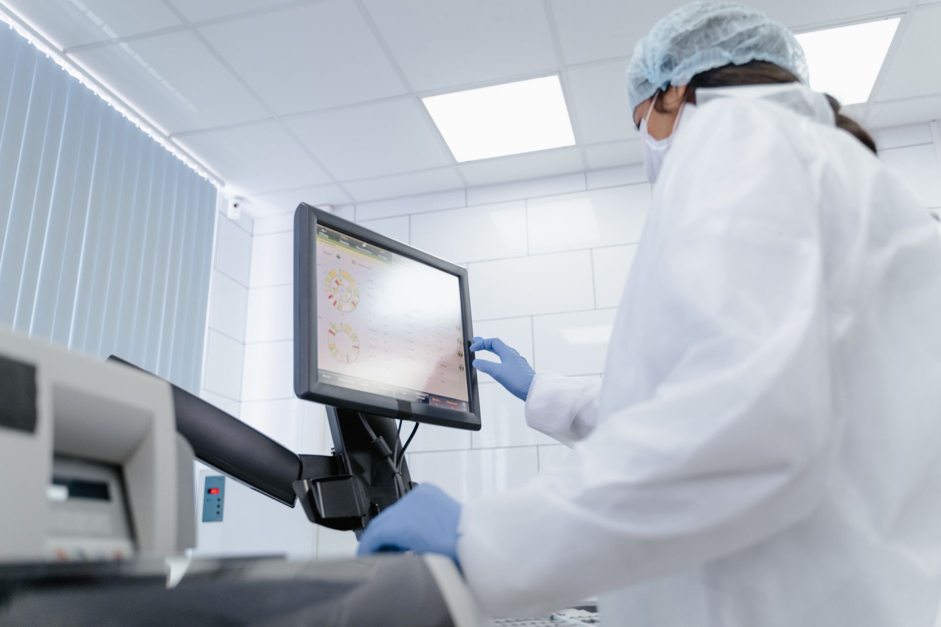 Woman in lab coat using touchscreen monitor in a modern laboratory setting.